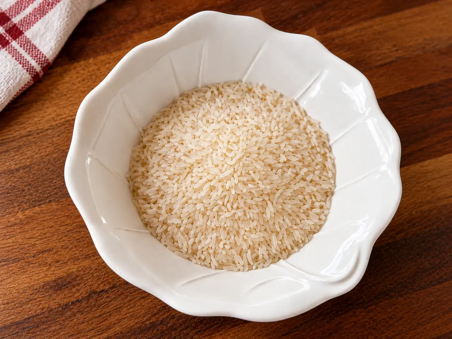Arroz Cru para Receita com Pernil Grãos de arroz cru em tigela branca sobre bancada escura.